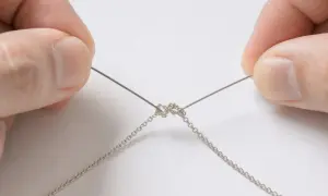 Manos sujetando un fino hilo metálico para desenredar una cadena de plata enredada.