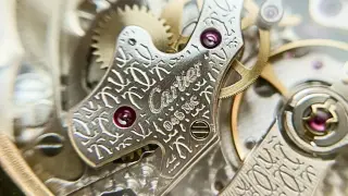 Detalle intrincado de un movimiento de reloj, con el grabado "Cartier" y un patrón de la joux perret. Engranajes dorados y rubíes visibles.