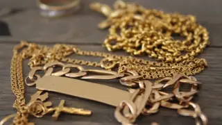 Varias cadenas y un anillo de oro sobre madera. ¿Cómo saber si una pulsera es de oro?