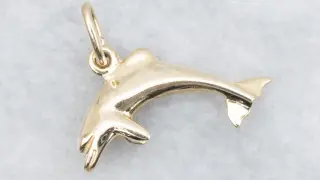 Un brillante colgante delfín oro, con detalles finos y un aro para colgar.