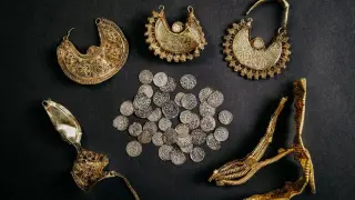 Tesoro de joyas de la Edad de los Metales: pendientes dorados ornamentados, monedas de plata antiguas y un fragmento de oro intrincado.