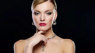 Elegante mujer con un conjunto collar y pendientes oro, labios rojos y mirada intensa.