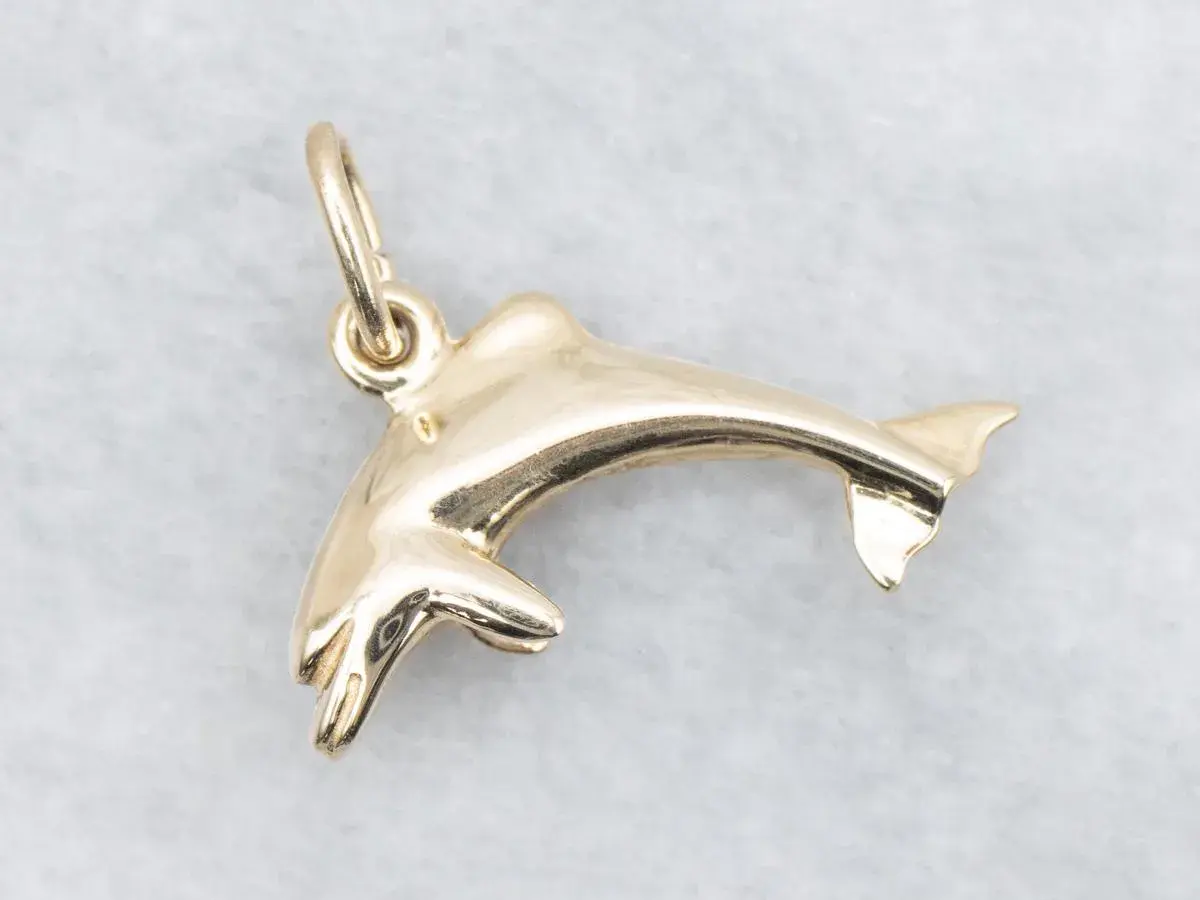 Un brillante colgante delfín oro, con detalles finos y un aro para colgar.