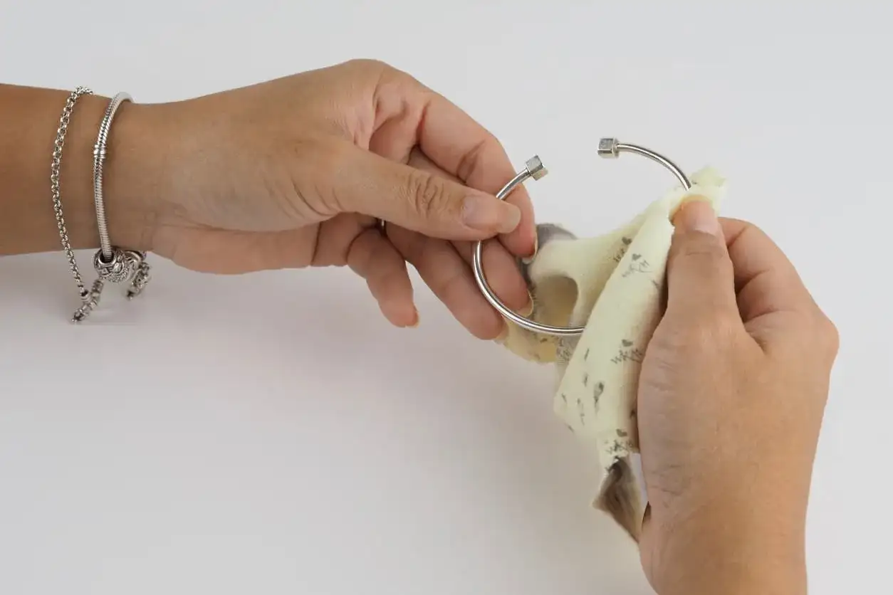 Manos limpiando una pulsera de plata con un paño. Aprende como limpiar la plata para que brille como nueva.