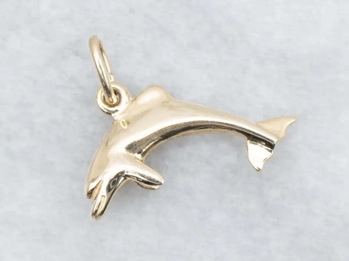 Un brillante colgante delfín oro, con detalles finos y un aro para colgar.