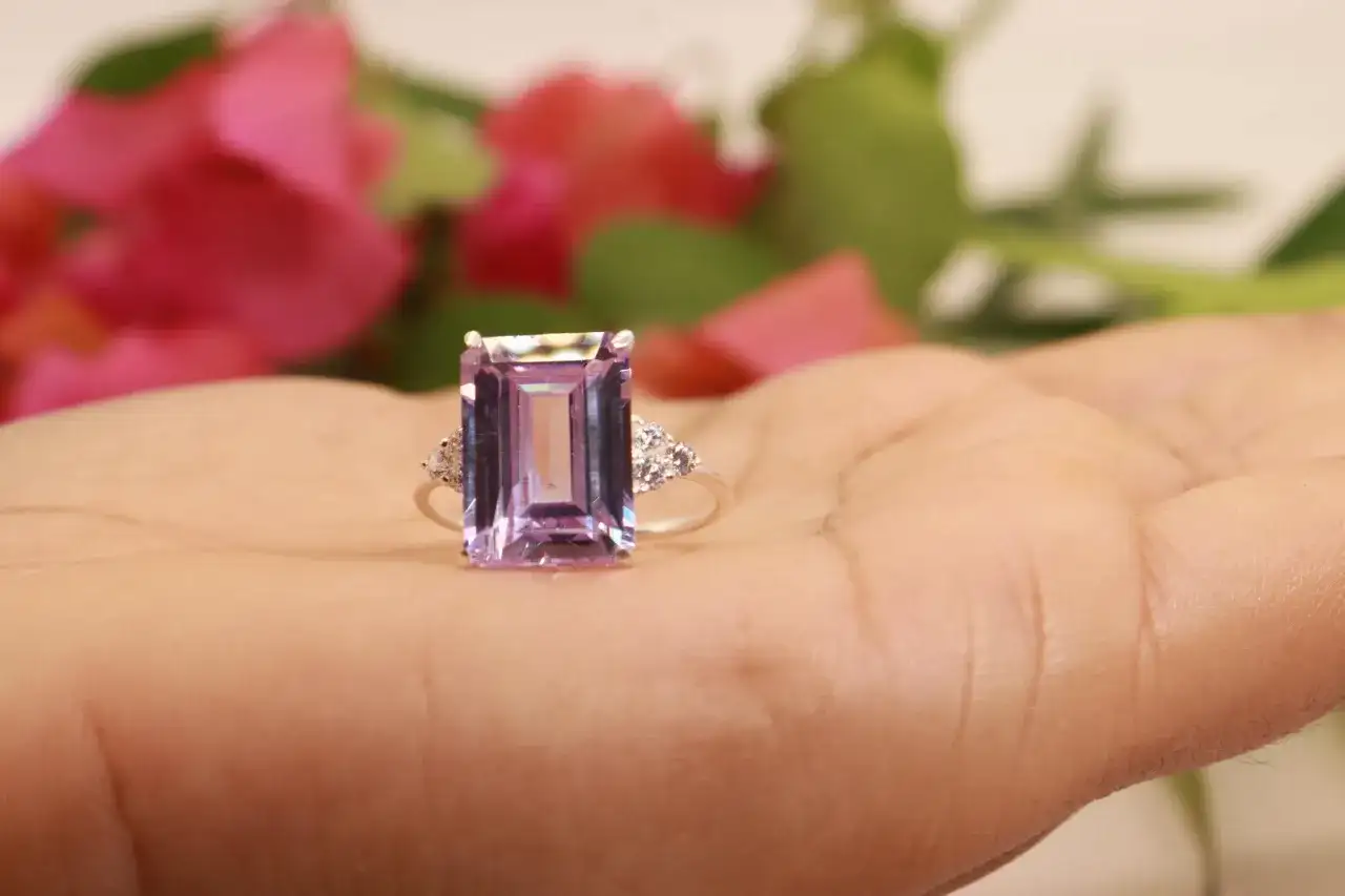 Anillo con gran piedra morada rectangular y pequeños diamantes a los lados, sobre una mano.