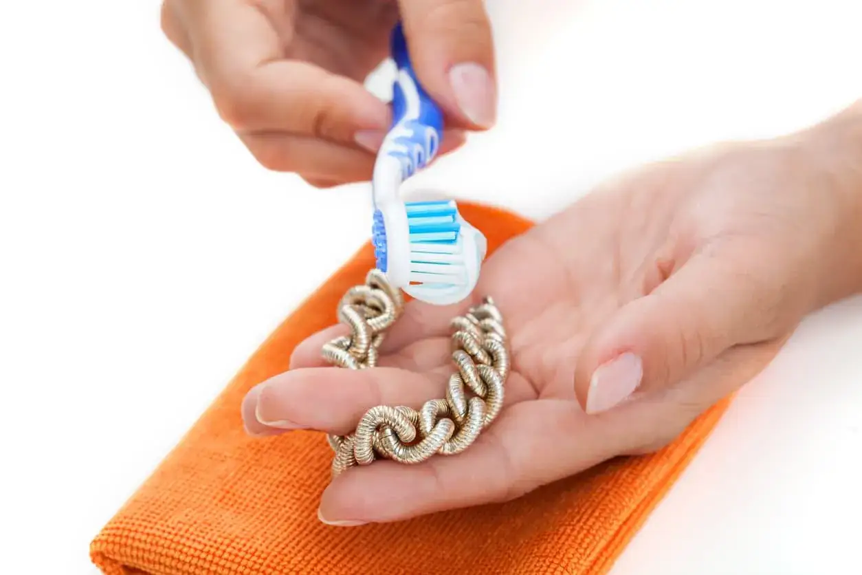 Manos limpiando una pulsera de oro con un cepillo de dientes. Aprende como limpiar el oro para que brille.