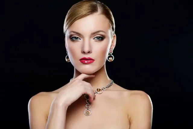 Elegante mujer con un conjunto collar y pendientes oro, labios rojos y mirada intensa.
